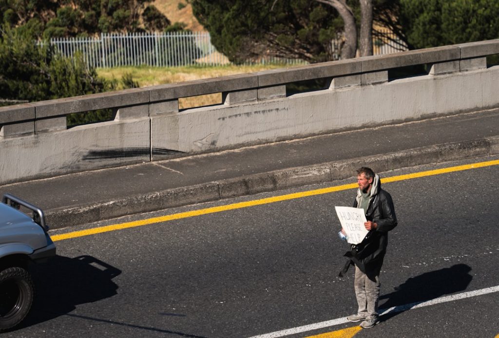 Um Homem Parado a Beira De Uma Estrada Segurando Um Pedaco De Papel sSMvbZ8021g