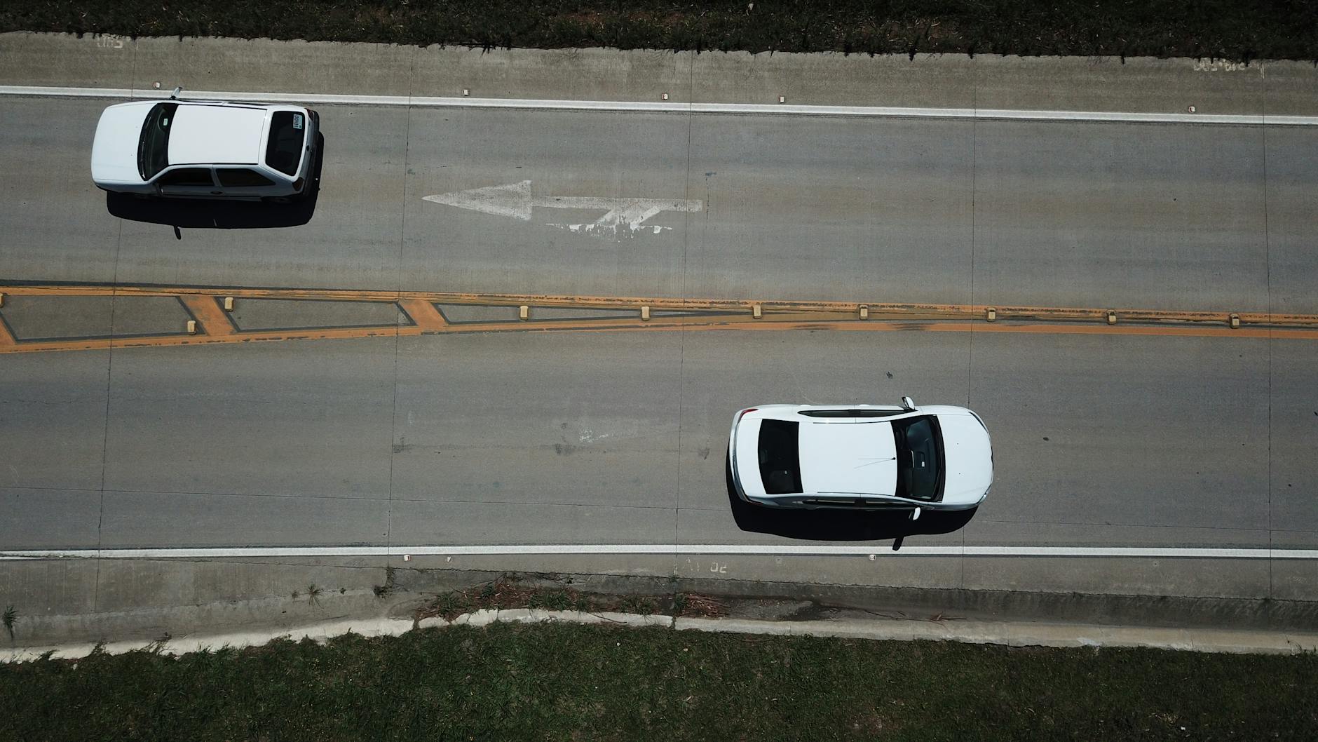 Aerial shot of two white cars on a highway with directional markings.