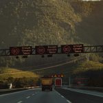Highway with speed limit signs against a mountainous backdrop and low traffic.