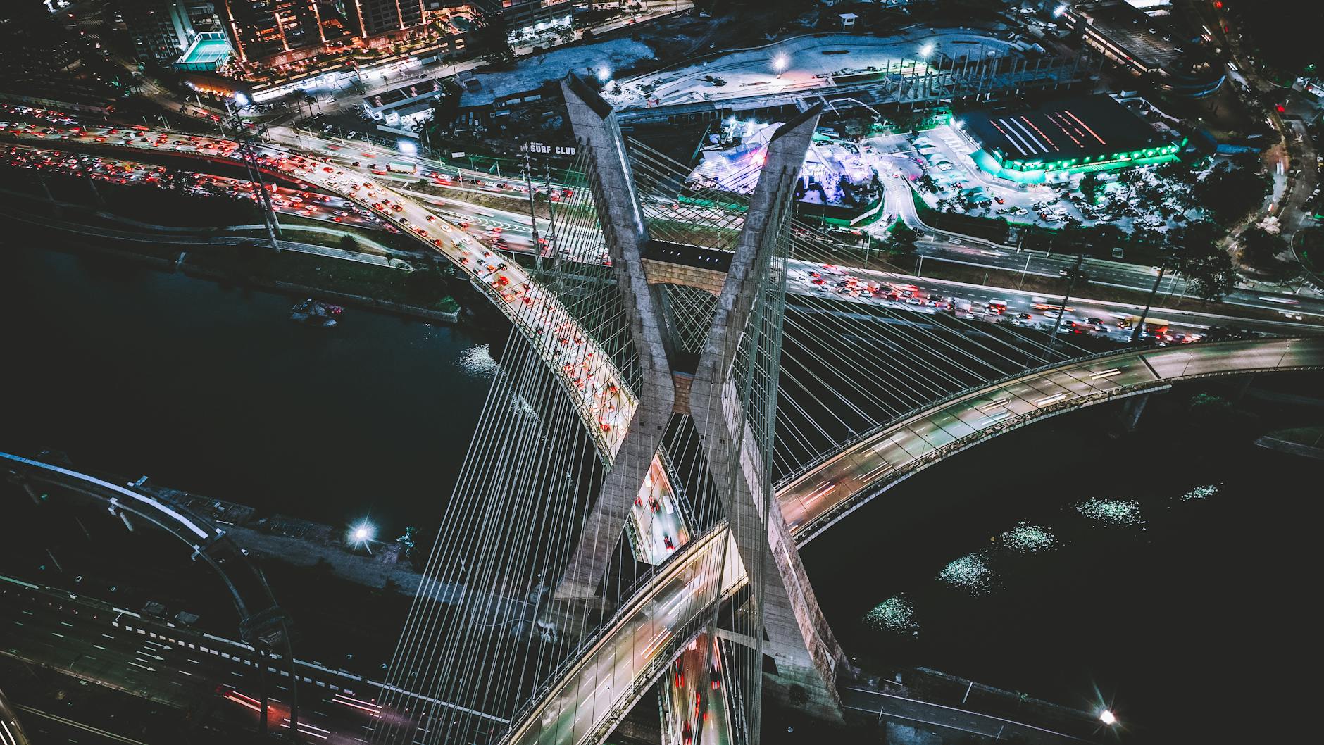 Aerial view of the iconic Estaiada Bridge in São Paulo at night, bustling with traffic and city lights.