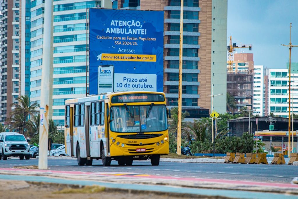 Um Onibus Amarelo Dirigindo Por Uma Rua Ao Lado De Predios Altos CSVIfPGAkB0