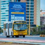 Um Onibus Amarelo Dirigindo Por Uma Rua Ao Lado De Predios Altos CSVIfPGAkB0
