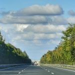 Scenic highway view with cloudy sky and symmetrical tree-lined road.