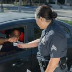 A police officer hands a ticket to a driver in a car on a sunny day street.
