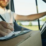 Close-up of a delivery driver inside a van writing on a clipboard. Logistics and service work concept.