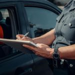 Close-up of a police officer writing a ticket by a car window. Law enforcement scene.