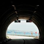 View from inside a tunnel opening to a scenic city landscape with clear skies.