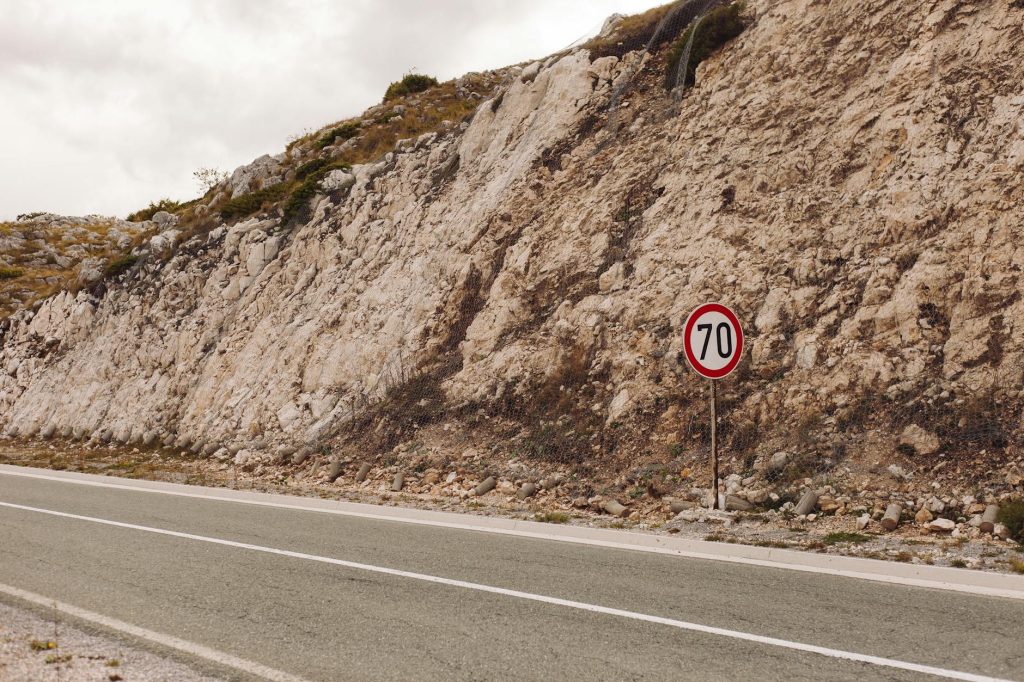A tarmac road along rocky terrain with a 70 speed limit sign on a cloudy day.
