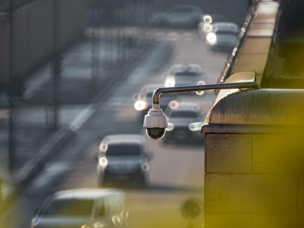 A security camera monitoring activity on a bustling city street with multiple cars in the background.