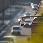 A security camera monitoring activity on a bustling city street with multiple cars in the background.