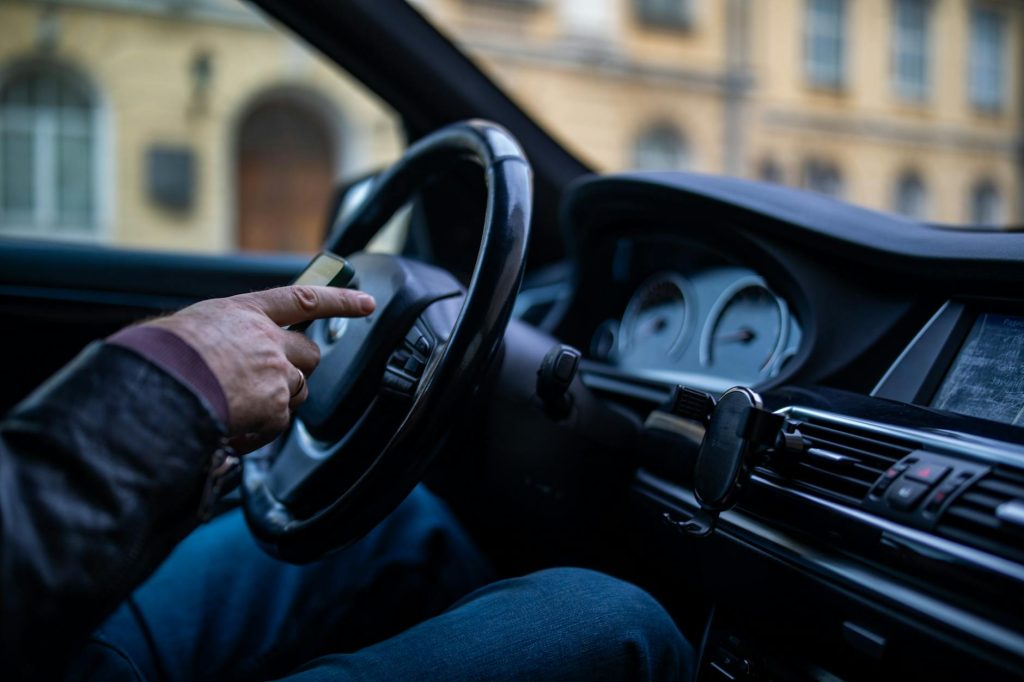 A man in a car interior using a smartphone while driving, emphasizing modern technology and lifestyle.