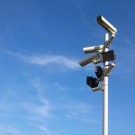Multiple security cameras on a pole with a clear blue sky backdrop.