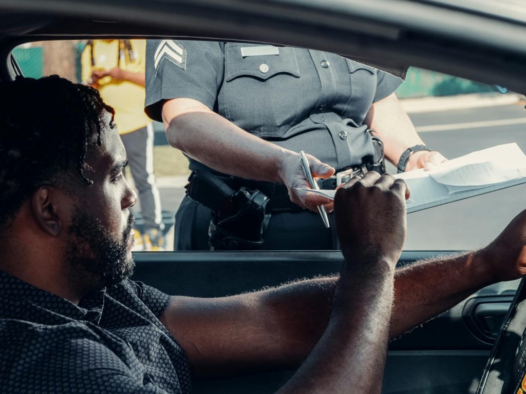 Police officer handing a traffic ticket to a driver during roadside inspection.