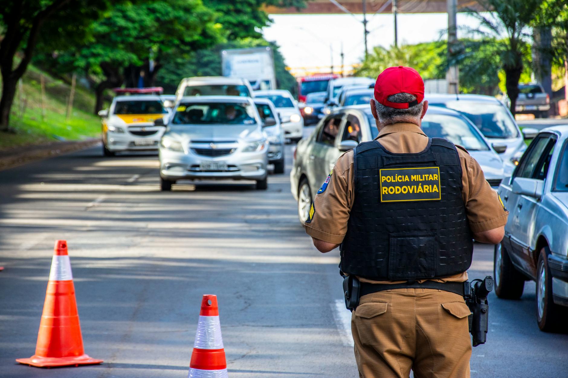 Police officer directing traffic in Londrina, Brazil with cars and cones on a busy street.