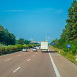 Cars and trucks driving on a highway surrounded by lush greenery and wind turbines.