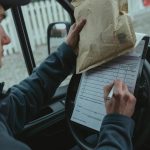 Courier signs delivery documents inside van while holding package, representing logistics and efficient mail service.