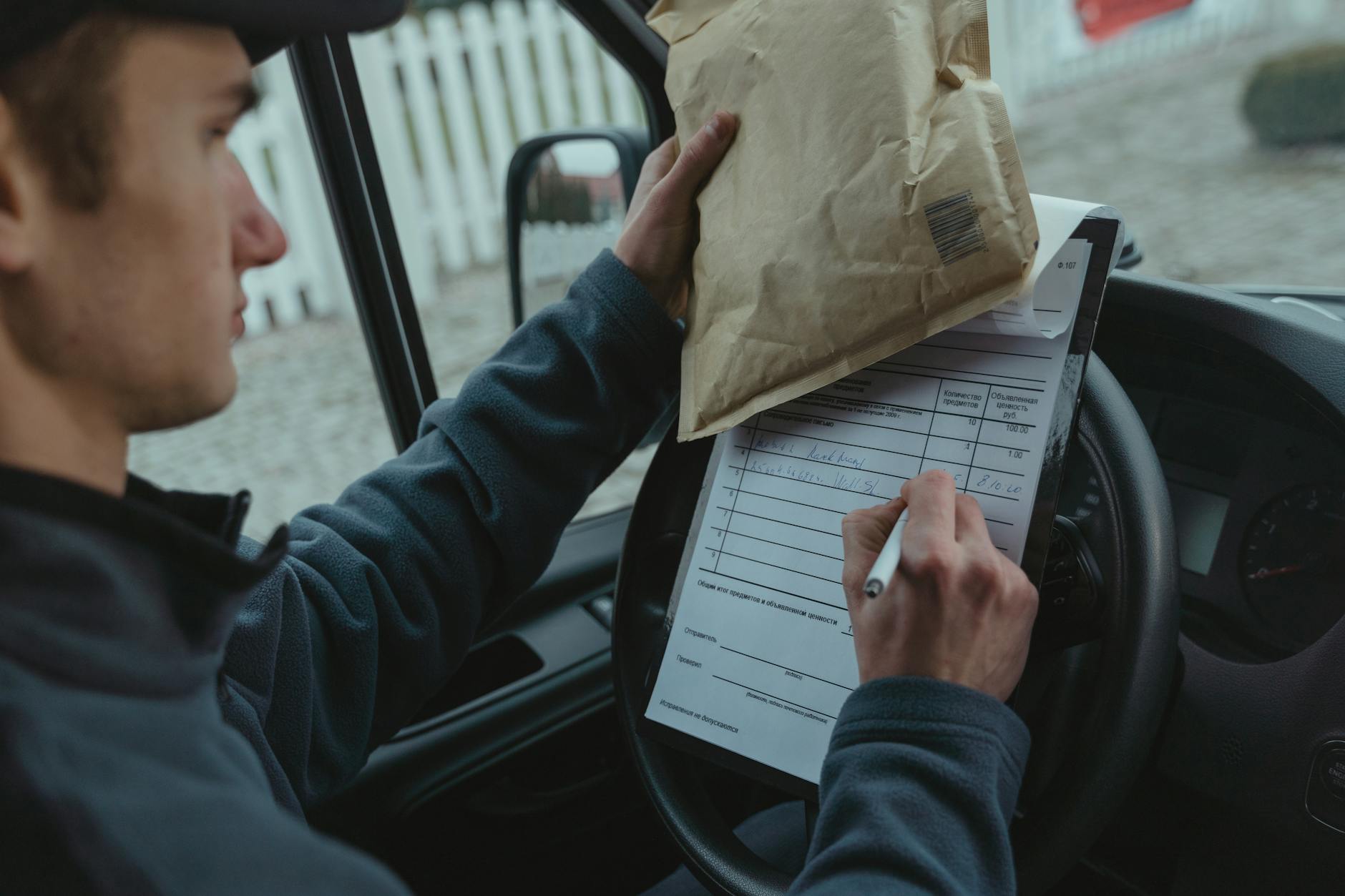 Courier signs delivery documents inside van while holding package, representing logistics and efficient mail service.