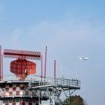 Radar tower and airplane in a blue sky, showcasing aviation technology