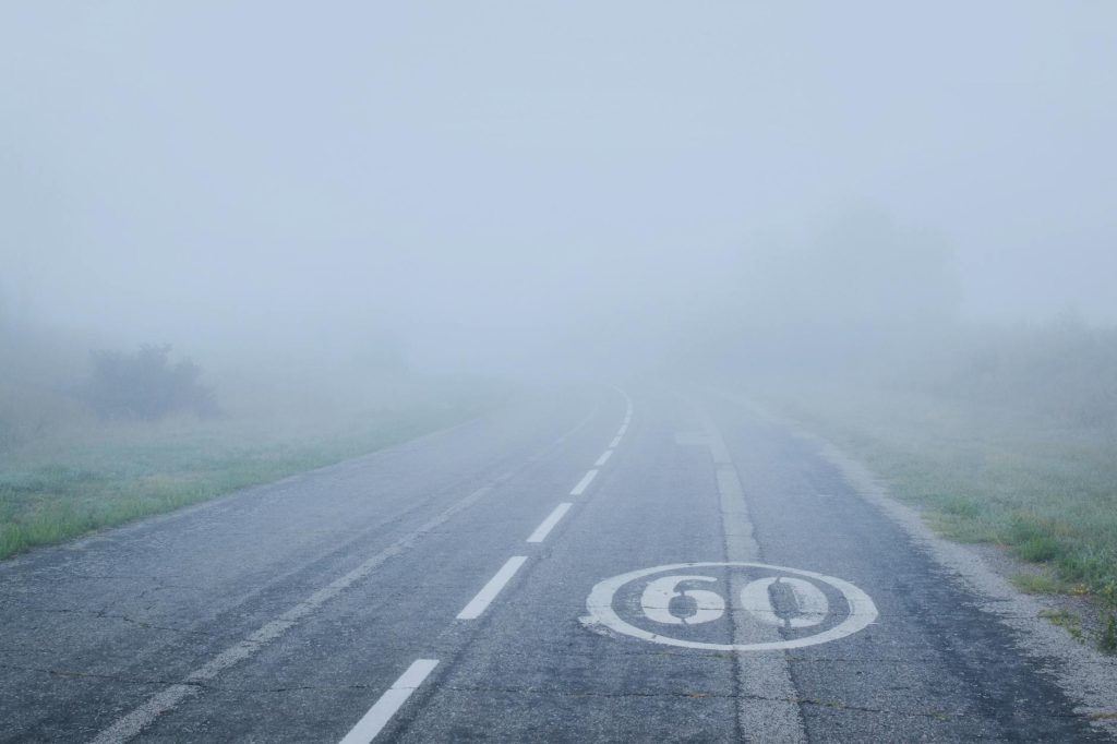 A foggy mountain road with a 60 km/h speed limit marking visible on the asphalt.