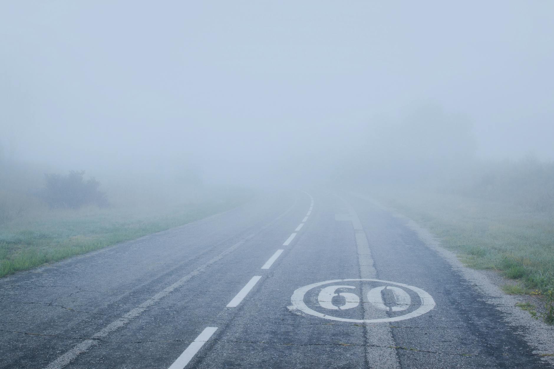 A foggy mountain road with a 60 km/h speed limit marking visible on the asphalt.
