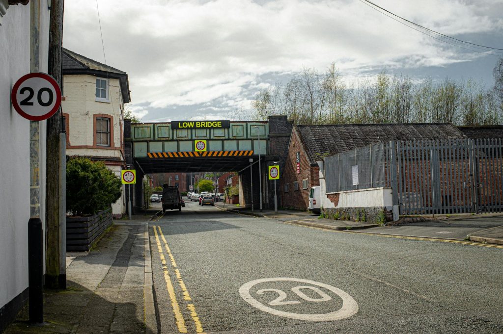 Street view in Liverpool featuring a low bridge and various traffic signs including speed limit indicators.