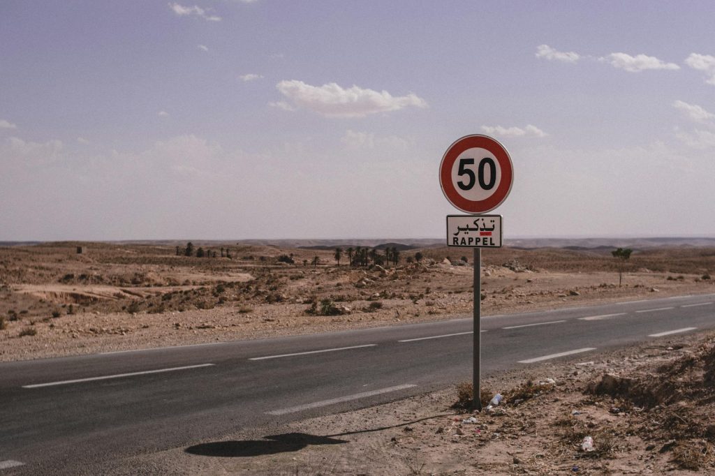 A deserted road in Tunisia marked with a 50 km/h speed limit sign under a clear sky.