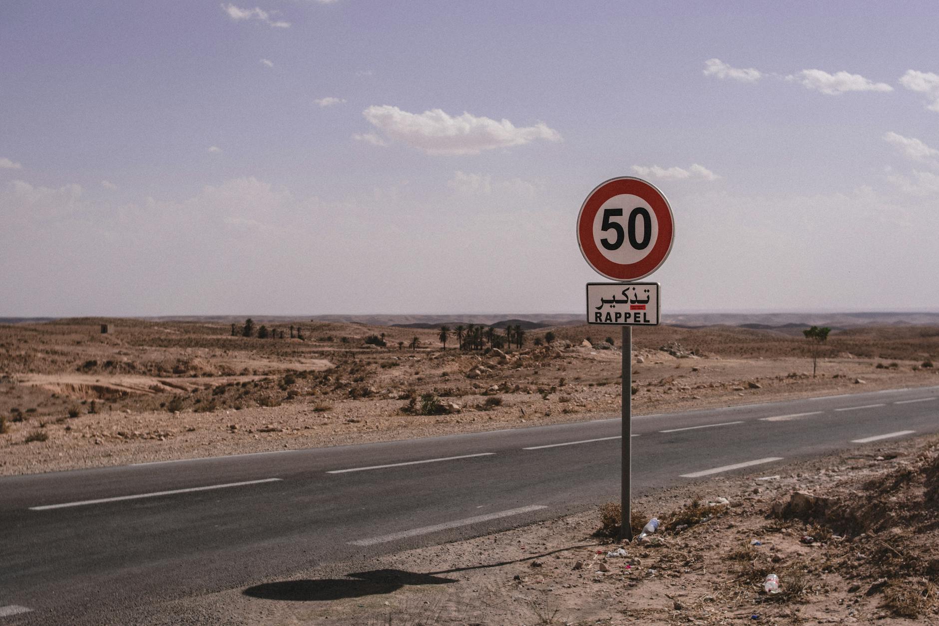 A deserted road in Tunisia marked with a 50 km/h speed limit sign under a clear sky.