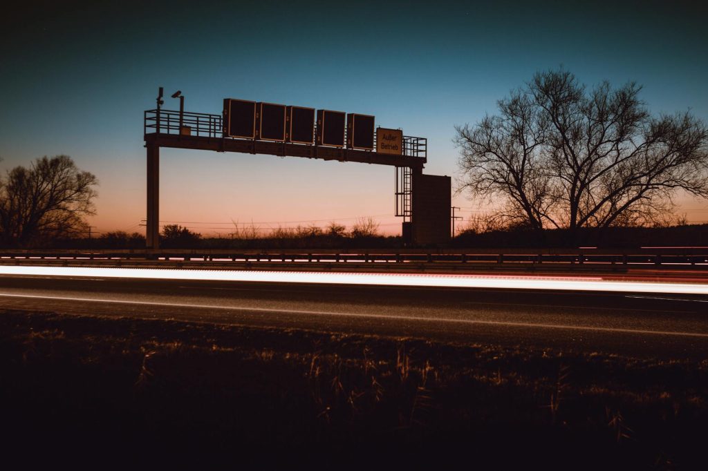 A striking long exposure of a highway at dusk featuring light trails and silhouetted trees.