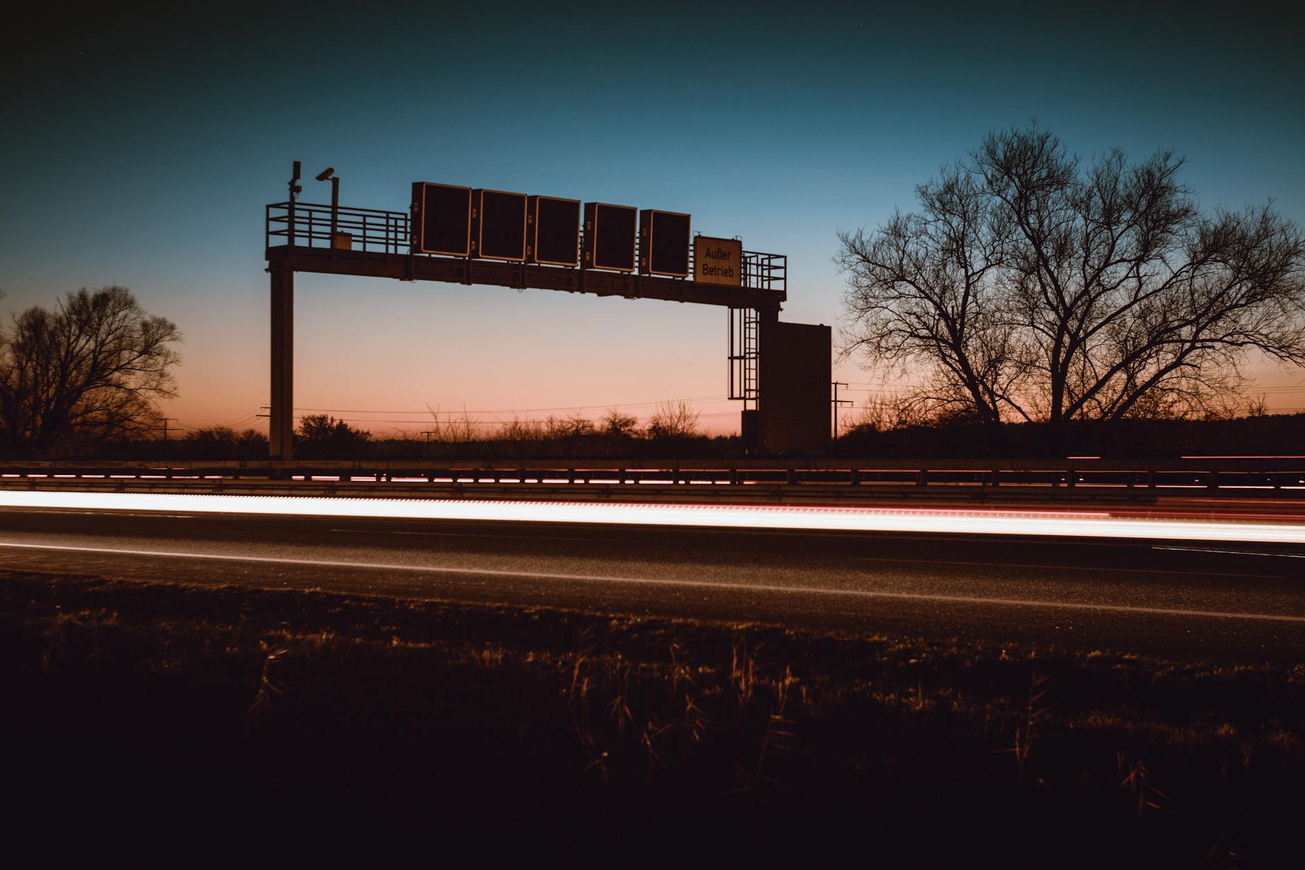 A striking long exposure of a highway at dusk featuring light trails and silhouetted trees.