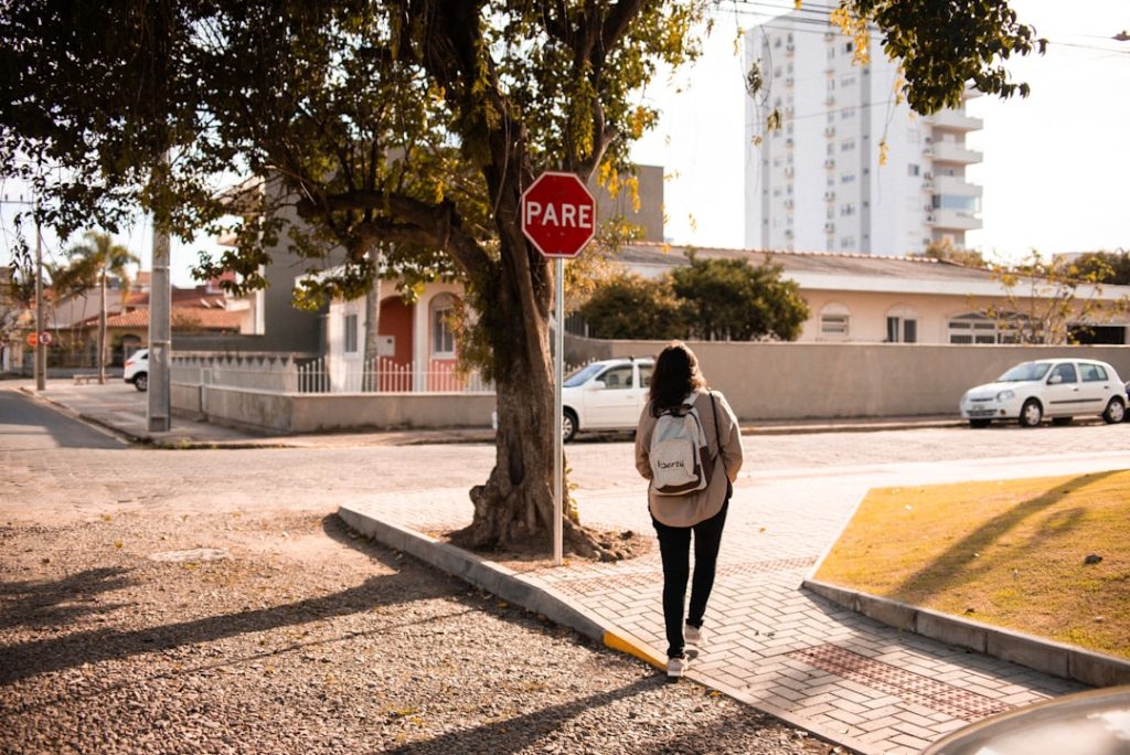 Uma Mulher Caminhando Por Uma Calcada Ao Lado De Um Sinal De Parada GCqabcbQ1qU