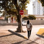 Uma Mulher Caminhando Por Uma Calcada Ao Lado De Um Sinal De Parada GCqabcbQ1qU