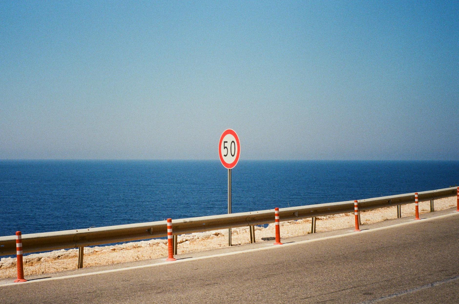 A scenic road along the ocean with a 50 km/h speed limit sign on a clear day.