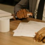 Close-up of a businessman holding and reviewing documents on a wooden desk.