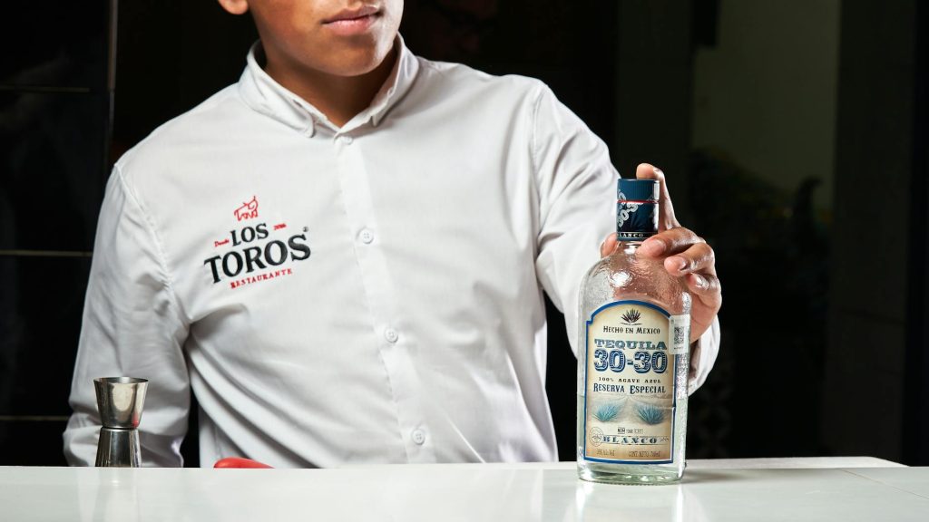 A bartender in Los Toros Restaurant displaying a bottle of Tequila 30-30, Reserva Especial.
