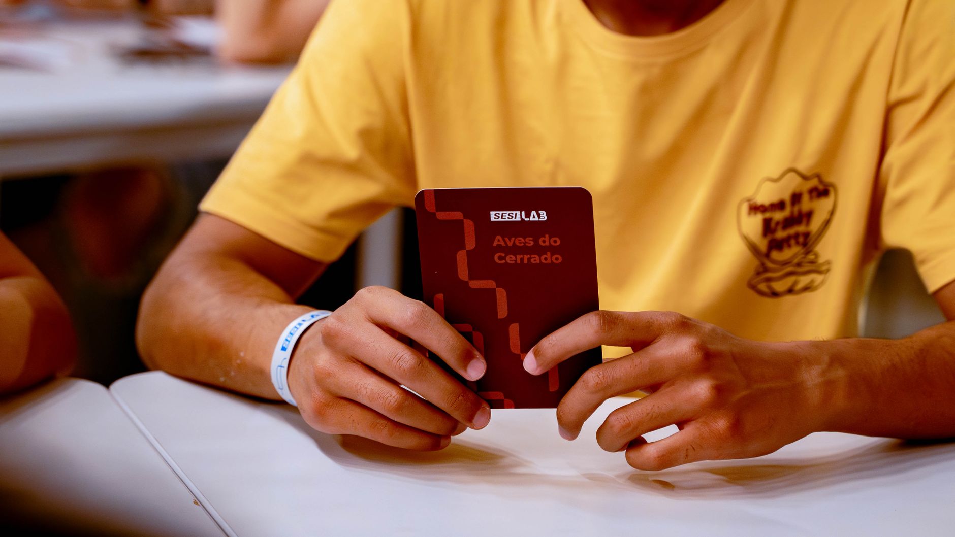 An adult holds the Aves do Cerrado booklet during an indoor educational event.