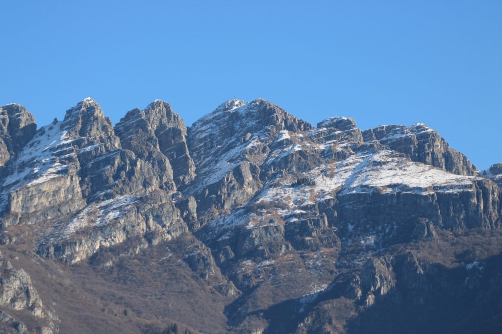 Breathtaking view of snow-covered mountain peaks in Lombardy, Italy under a clear blue sky.