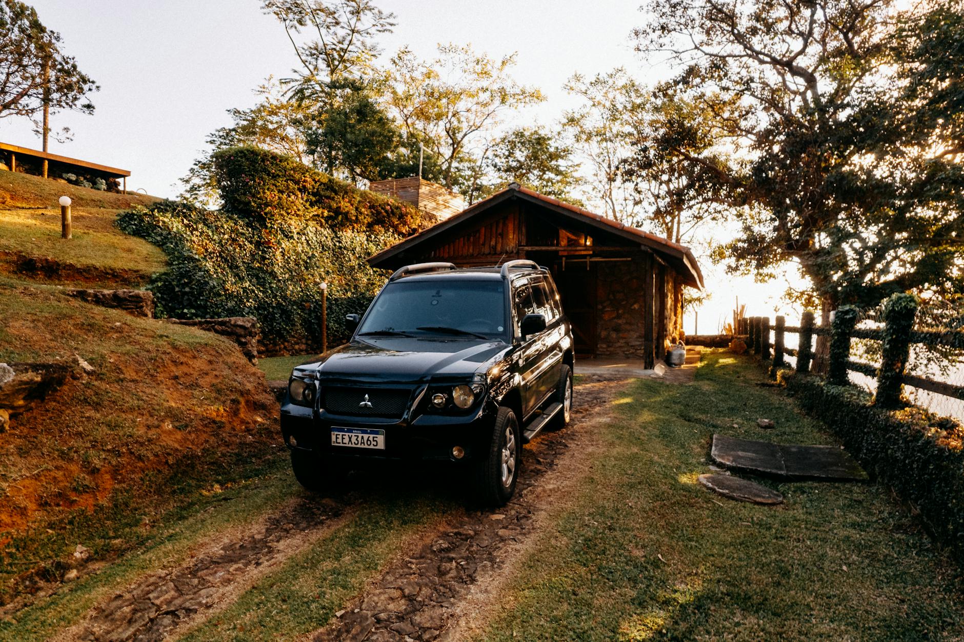 A black SUV parked outside a rustic cabin in the scenic countryside during sunset.