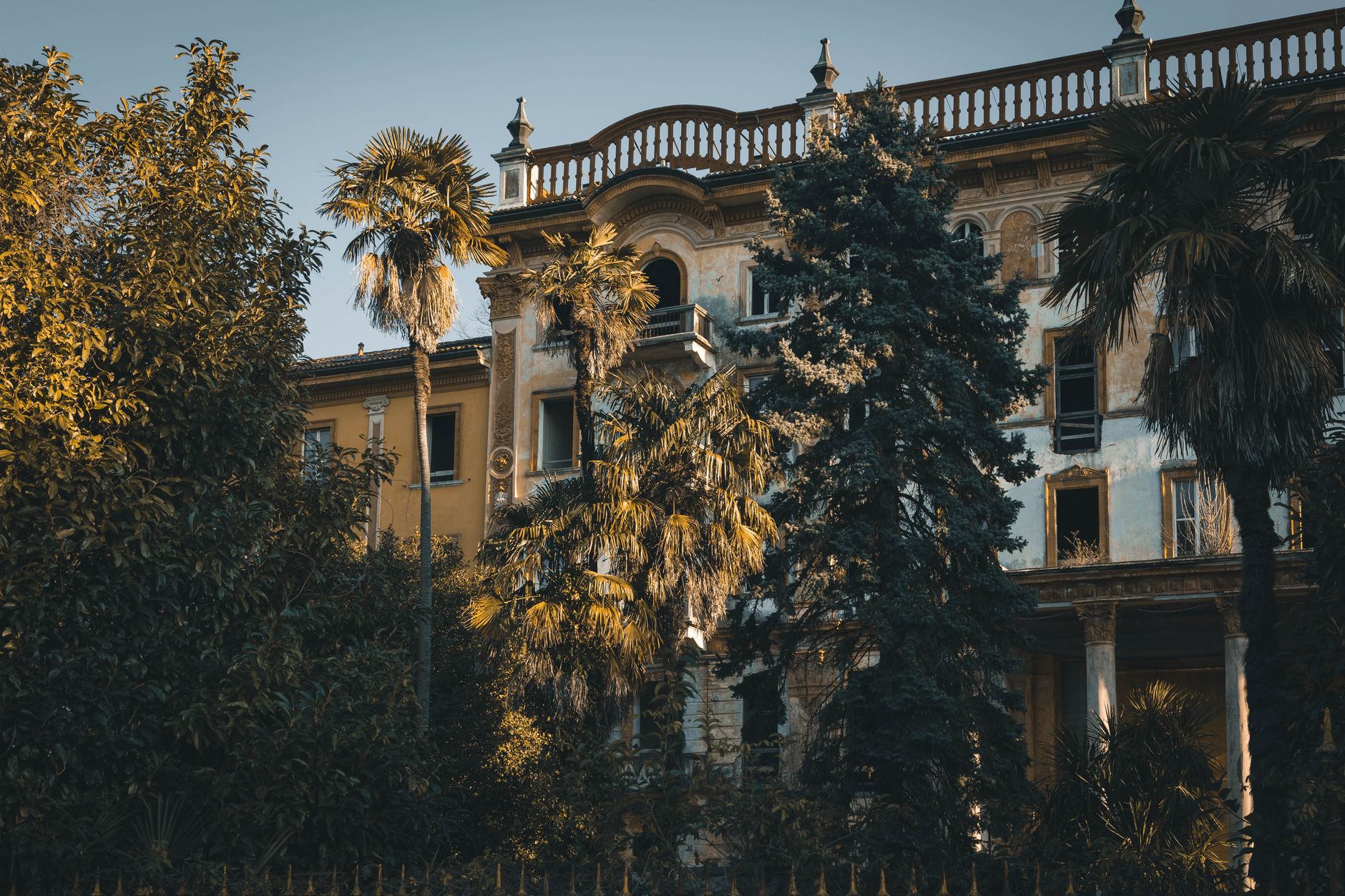 A mysterious abandoned villa surrounded by lush trees in a warm sunset light.