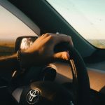 A serene drive at sunrise showcasing a hand on the steering wheel in a relaxed atmosphere.