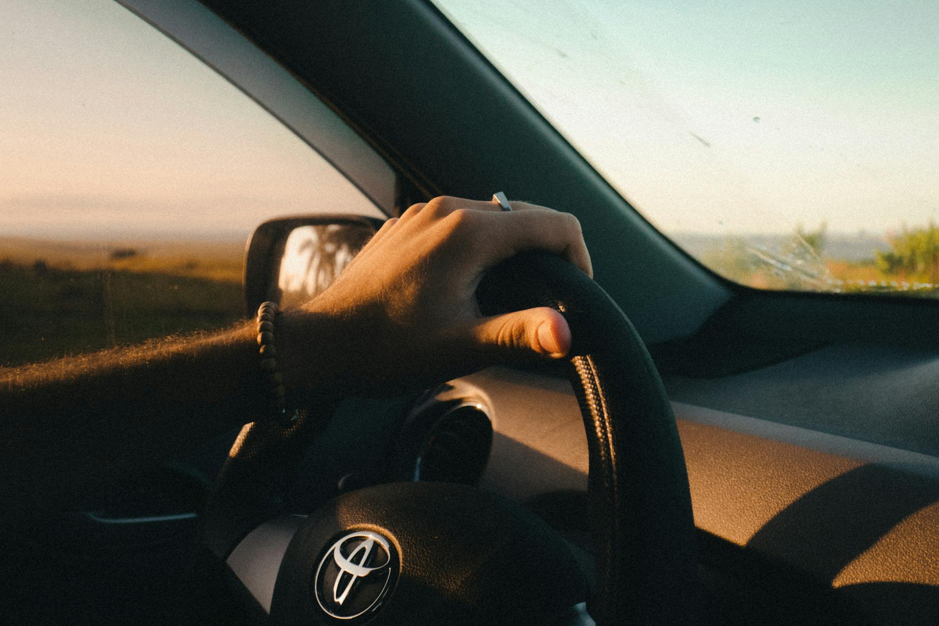 A serene drive at sunrise showcasing a hand on the steering wheel in a relaxed atmosphere.