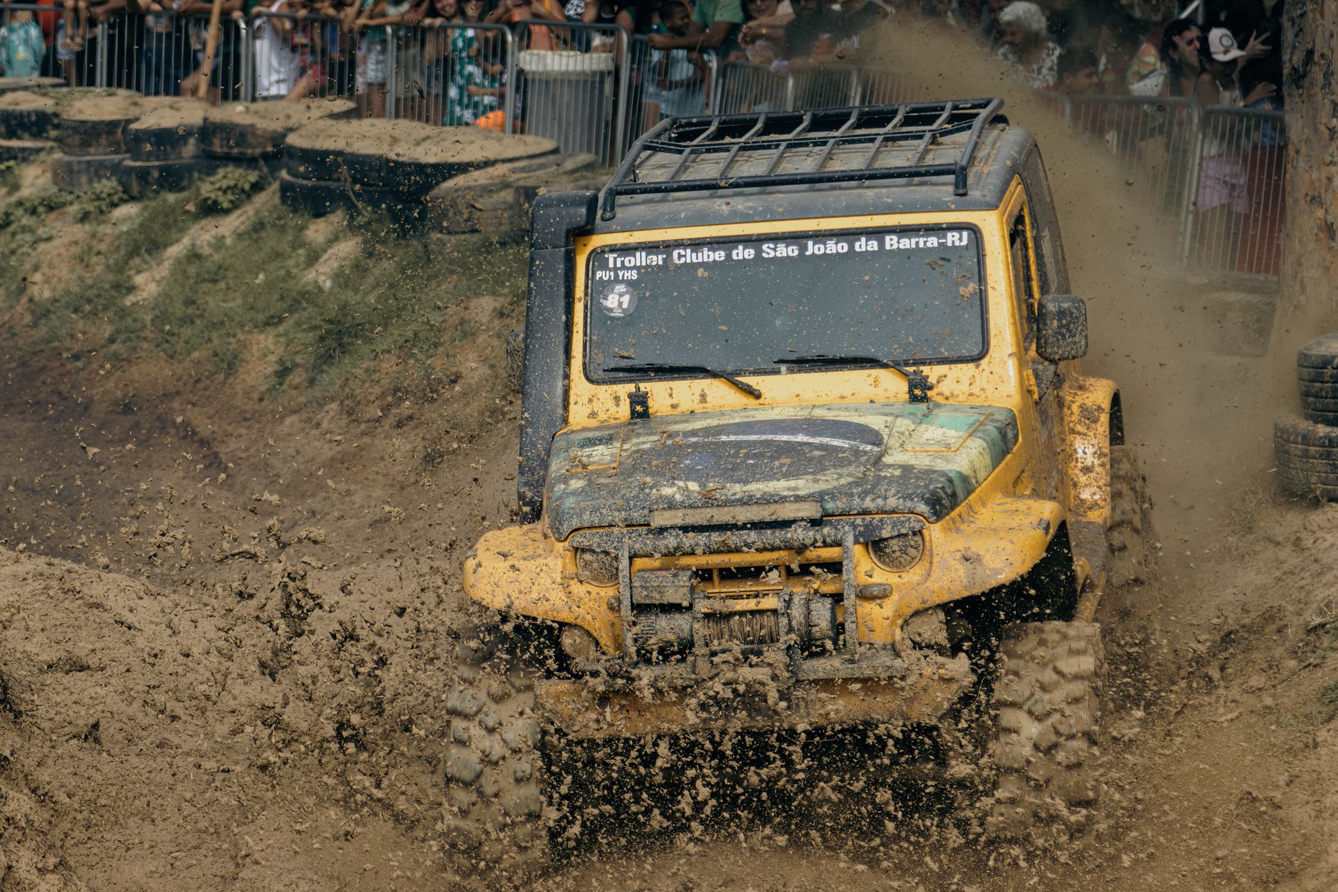 Muddy SUV competes in an exciting off-road race event with spectators watching.