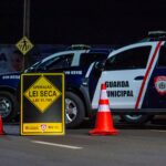 Night scene of a traffic checkpoint by the Municipal Guard in Londrina, Brasil, featuring police vehicles and cones.