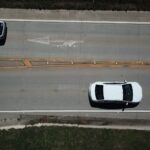 Aerial shot of two white cars on a highway with directional markings.