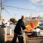 Two workers handling waste disposal in an urban environment on a sunny day.