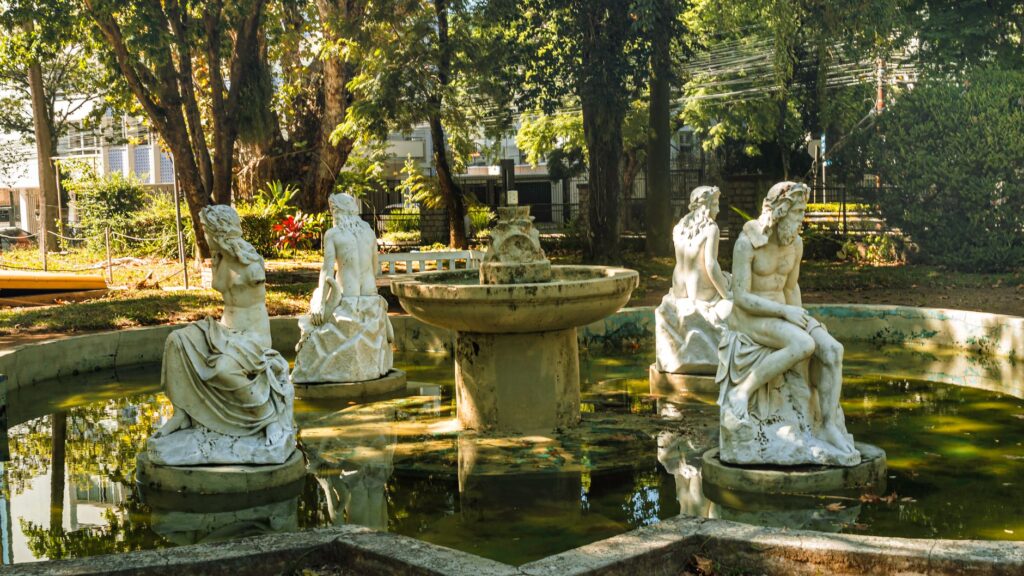 Elegant white statues encircle a fountain in a peaceful outdoor garden.