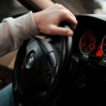 Close-up view of hand gripping the steering wheel, showcasing the car's dashboard and interior design.