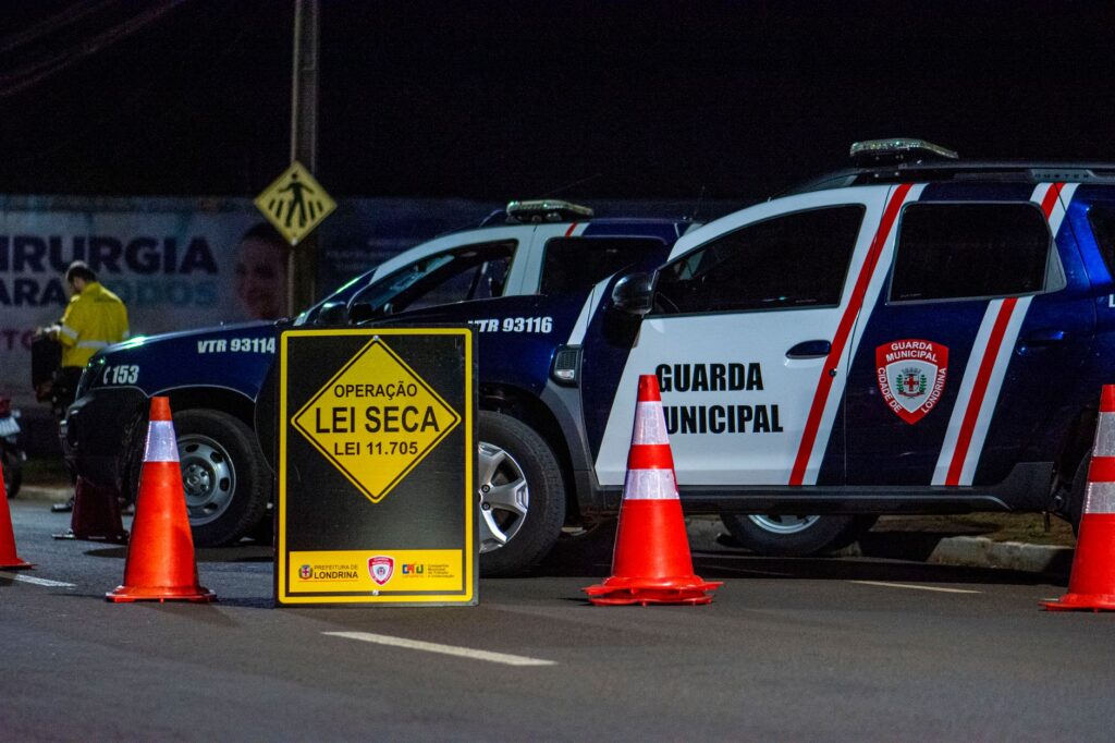 Night scene of a traffic checkpoint by the Municipal Guard in Londrina, Brasil, featuring police vehicles and cones.