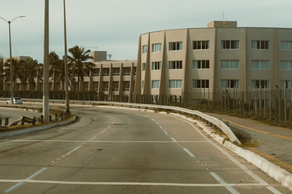 Curved road leading to a modern apartment building in Natal, Brazil, surrounded by palm trees.