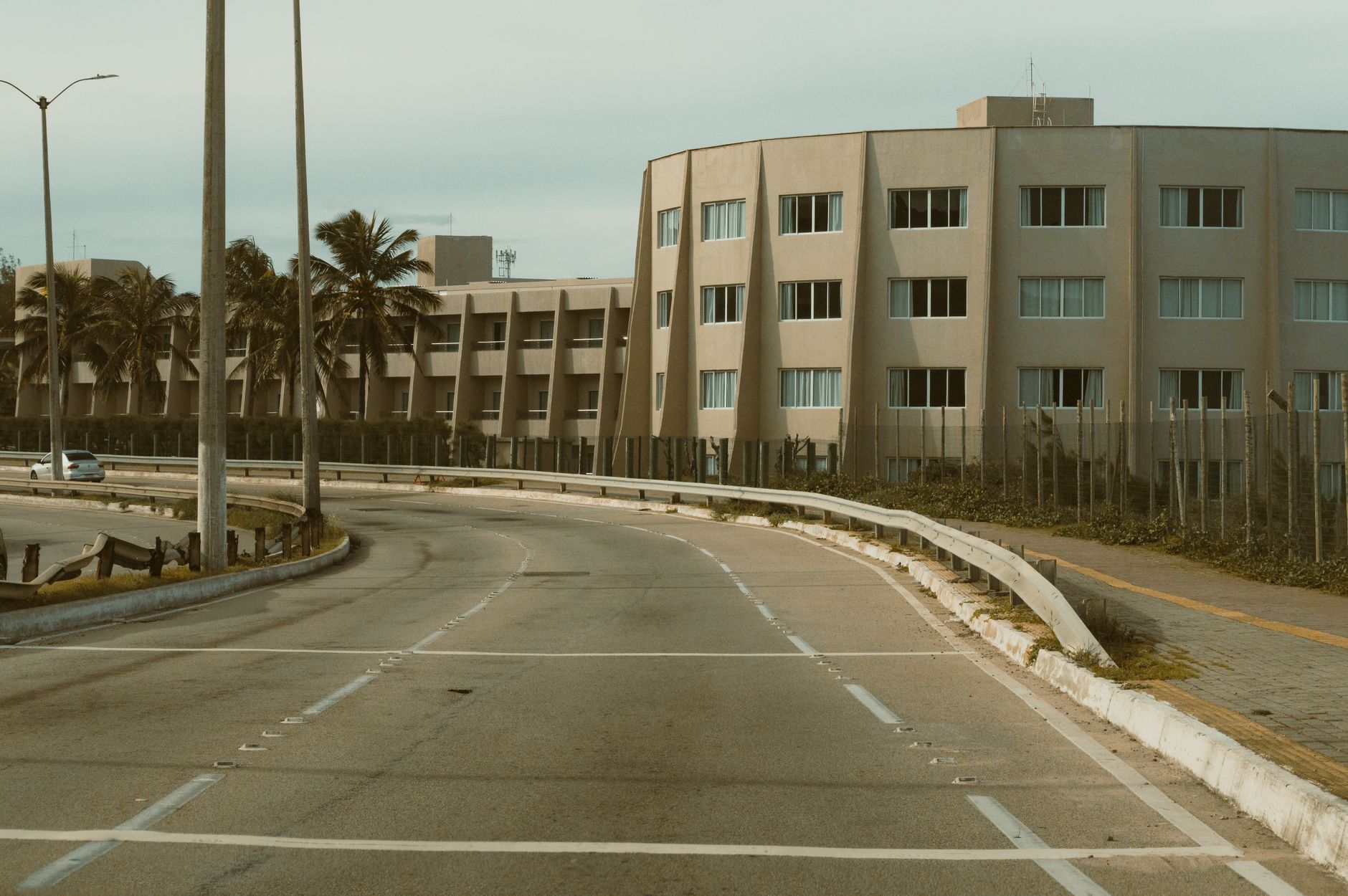 Curved road leading to a modern apartment building in Natal, Brazil, surrounded by palm trees.
