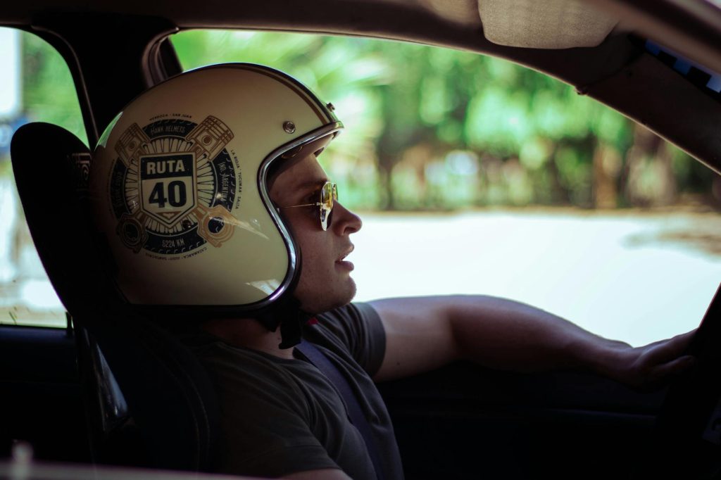 Man wearing a Ruta 40 helmet driving a car, looking into the distance.